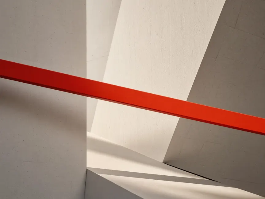 Abstract architecture: a single red-orange beam running straight through pale concrete planes